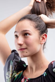 Young woman putting her long brunette hair into a ponytail holding it neatly above her head with her hands in close up