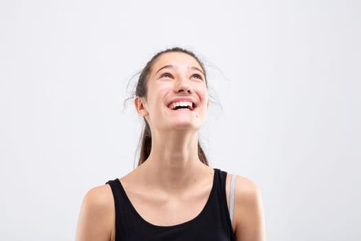 Elated laughing happy young woman looking up with a beaming toothy smile in a head and shoulders portrait on white