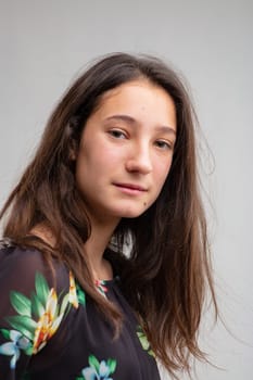 Thoughtful young woman looking quietly at camera in a half turned head portrait over grey