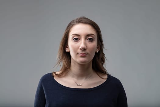 Serious attractive middle-aged woman with shoulder length hair wearing a black top over a grey background