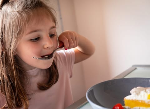 Pretty little girl enjoying a mouthful of cake eating off the spoon as she sits at table in a close up portrait