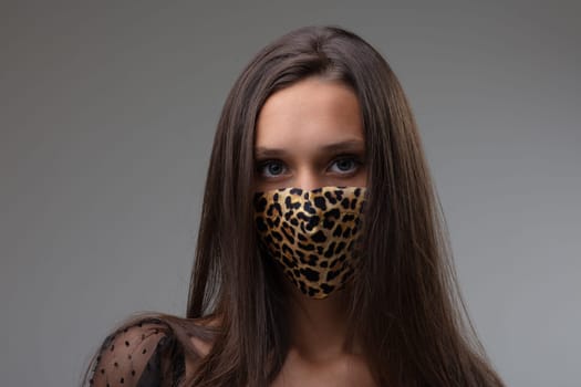Woman wearing a fashionable animal print face mask as protection against the coronavirus during the Covid-19 pandemic against a grey background in a frontal portrait