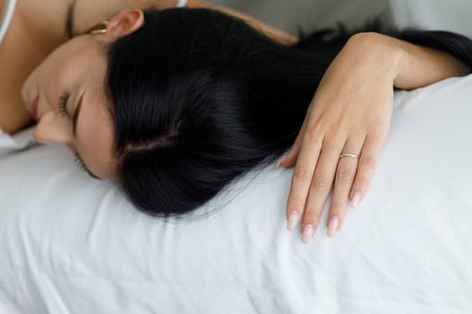 Exhausted young woman passed out sleeping on a white sofa or bed in close up on her hand and top of her head with copyspace