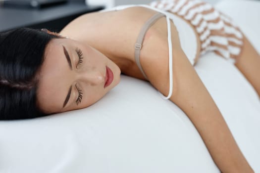 Exhausted young woman enjoying a refreshing sleep with her arm draped over the sofa and a close up on her serene face with closed eyes in a head to toe view