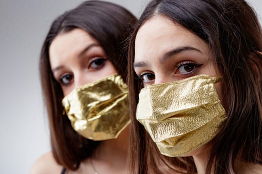 women wearing GOLDEN protective face masks watching you, young woman good looking and lucky in golden facial covers protect from COVID-19 coronavirus on a neutral babkcround, affordable healthcare concept