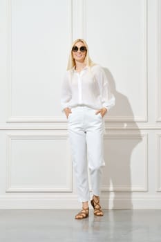 Cheerful woman in white cotton shirt, sunglasses and trousers posing indoors