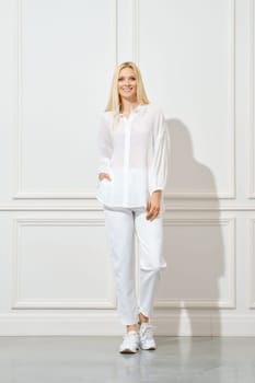 Smiling woman in white cotton shirt and trousers with pockets posing