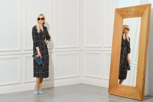 Gorgeous woman posing in long black wool dress in the room near the large mirror