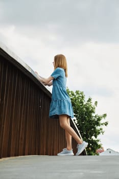 Woman in jeans dress leaning on railing of a bridge