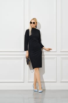Casual office female outfit. Serious businesswoman in sunglasses and tight black dress with handbag