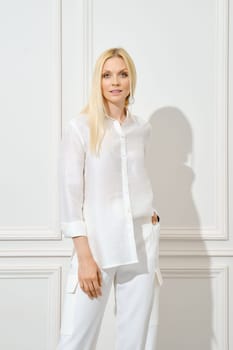 Portrait of pretty blonde woman in cotton shirt standing by white wall
