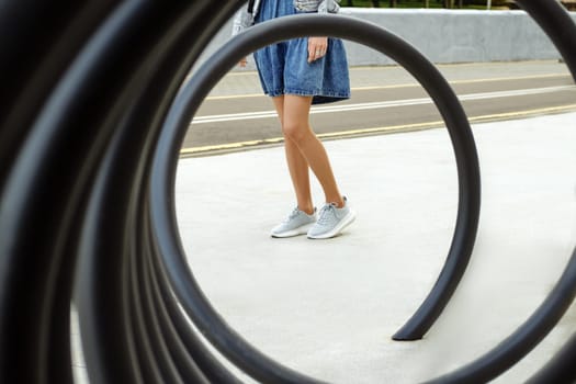 View through metal spiral on legs of unrecognizable woman in beige tights and sneakers