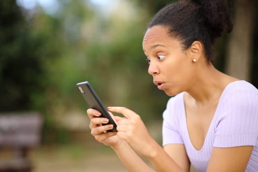 Amazed black woman checking phone content in a park