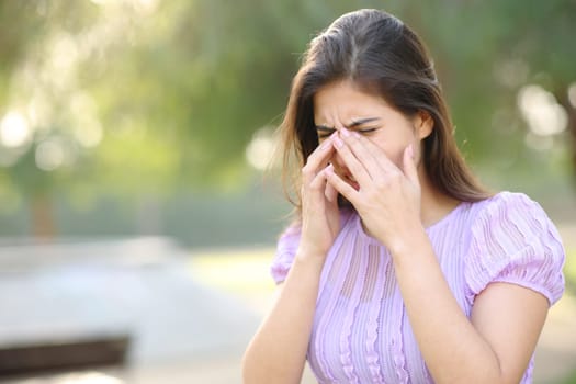 Allergic woman scratching eyes in summer in a park