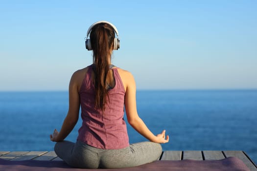 Back view of a yogi doing yoga with headphone on the beach