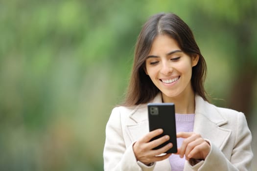 Front view portrait of a happy woman walking using cell phone in winter