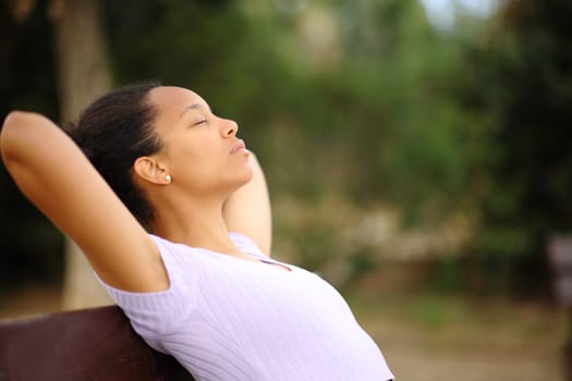 Profile of a relaxed black woman resting with hands on head sitting in a park