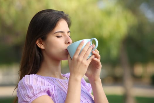 Woman drinking coffee standing in a park alone