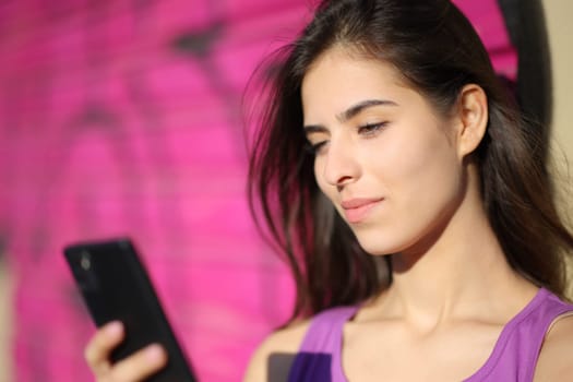 Beautiful woman checking phone leaning in a violet wall
