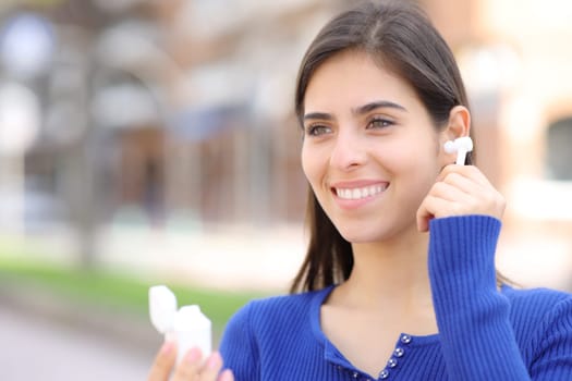 Happy woman putting on earbud on ear walking in the street