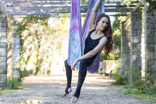 Smiling woman sits in yoga hammock. Mid shot