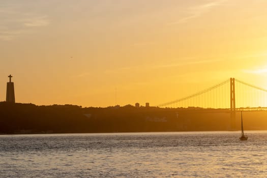 Orange sunset over the Tagus River - the statue of Jesus christ and the bridge over the river. Mid shot