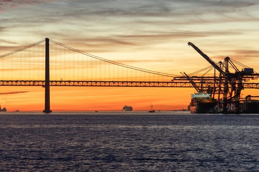 Lisbon and 25th of April Bridge at sunset - industrial cranes working by the water. Mid shot