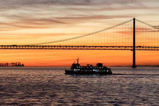 Lisbon and 25th of April Bridge at sunset - the transport ship sails on the Tagus River. Mid shot