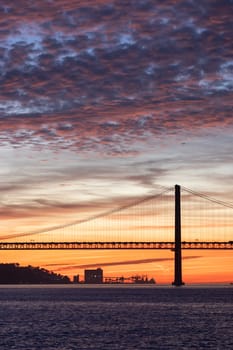 Lisbon 25th of April Bridge at sunset and industrial cranes at the background. Vertical shot