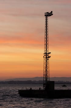 Electric tower on the water at an orange sunset. Mid shot