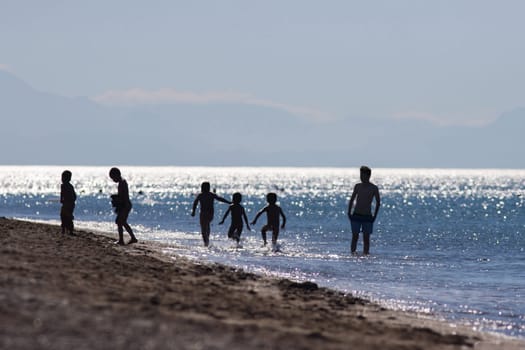 Defocused silhouettes of beach in Antalya, Turkey. Group of people - adult and childs spend time on the sea - swiming and playing - summer and hot, Mountans on the background