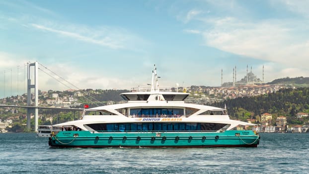 Istanbul, Turkey - May 7, 2023: Modern ferry boat sailing in Bosphorus Strait with Bosphorus bridge and Camlica Mosque in the background