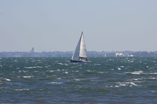 Sailboat sails the blue sea at grey weather. Mid shot