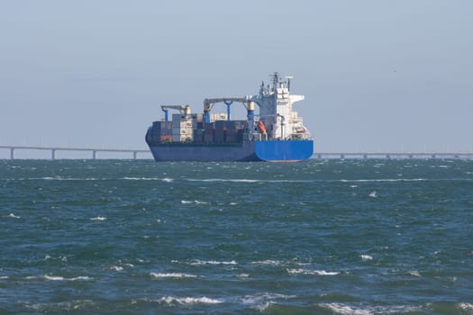 A big cargo ship sails the sea to the bridge. Mid shot