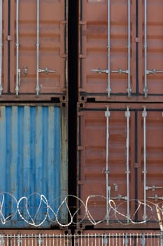 Multi colored cargo containers behind the wire fence. Vertical shot