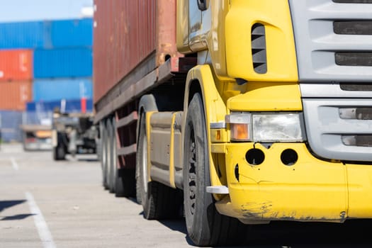 Scratched yellow truck stands in the parking lot at the warehouse with containers. Mid shot