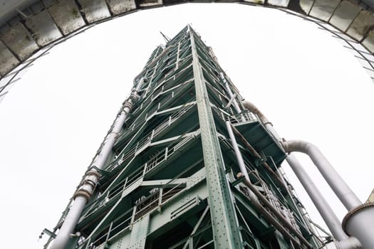 A tall oil refining tower against a gray sky. Mid shot