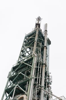 High oil and gas processing tower on a background of grey sky. Vertical shot