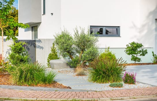The frontyard of a modern house, garden details with colorful plants, dry grass beds surrounded by grey rocks.