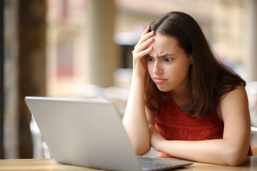 Frustrated woman cheking laptop after mistake in a bar terrace