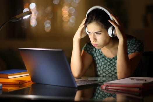 Stressed student e-learning with laptop and headphone in the night at home