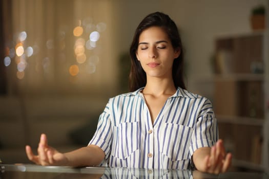 Woman relieving stress doing yoga in a desk in the night at home