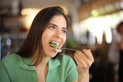 Woman eating lettuce in a restaurant looking away