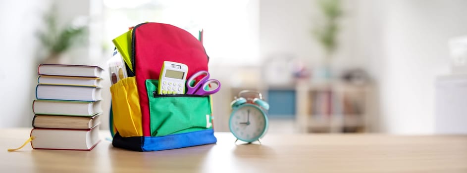 Colourful backpack with stationery standing on the table indoors. Concept of back to school.
