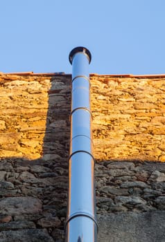 Chromed metal smokestack attached to a dry stone wall. Sunset light