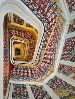 Abstract shape luxurious stairs with red carpet cover and golden handrail. Hypnotic pattern swirl staircase with mirror reflections on the stairwell walls