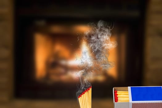 Matches, fire and smoke. A matchbox and rising smoke from several extinguished matches against an abstract blurred fireplace background. Space for copying.