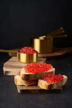 Red caviar on slices of white wheat bread on a black table, concept of luxury and gourmet cuisine
