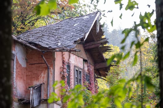An old house ruin with a derelict roof, seen from between trees, Bled in Slovenia