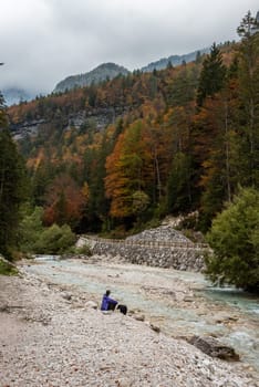 A hiker resting with his dog at a lake in the Bistrice valley, enjoying the view on the Julian Alps, Slovenia